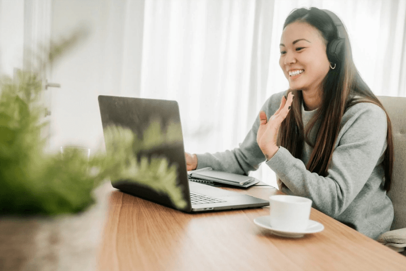 Happy woman working from home with headphones and laptop in a bright, comfortable space